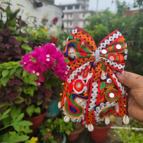 Colorful Navratri hair bow with intricate multicolor threadwork, mirror embellishments, cowrie shells, and decorative charms