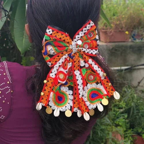 Colorful Navratri hair bow with intricate multicolor threadwork, mirror embellishments, cowrie shells, and decorative charms