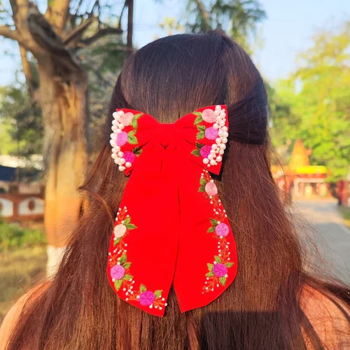 Red fabric hair bow with floral embroidery, pearl embellishments, and long ribbon tails